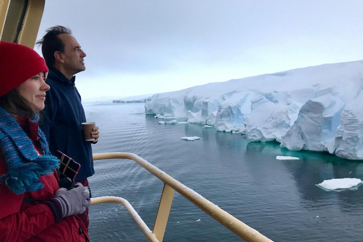 Man and woman looking at Antarctic ice from deck of boat