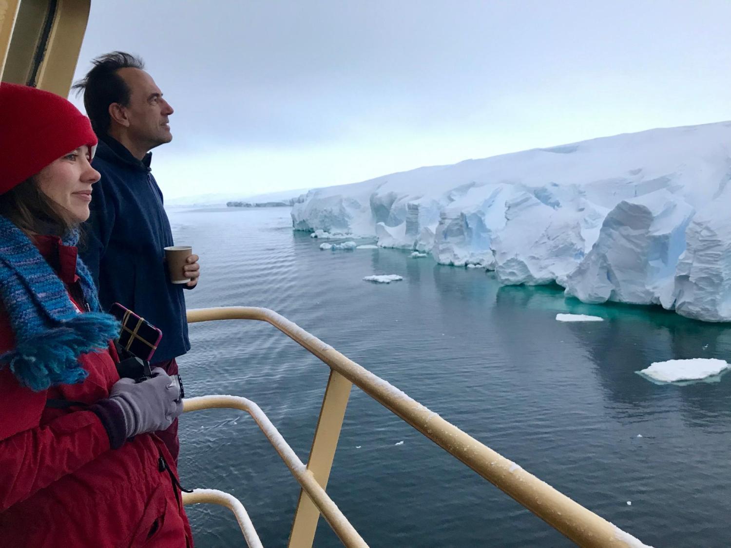 Man and woman looking at Antarctic ice from deck of boat