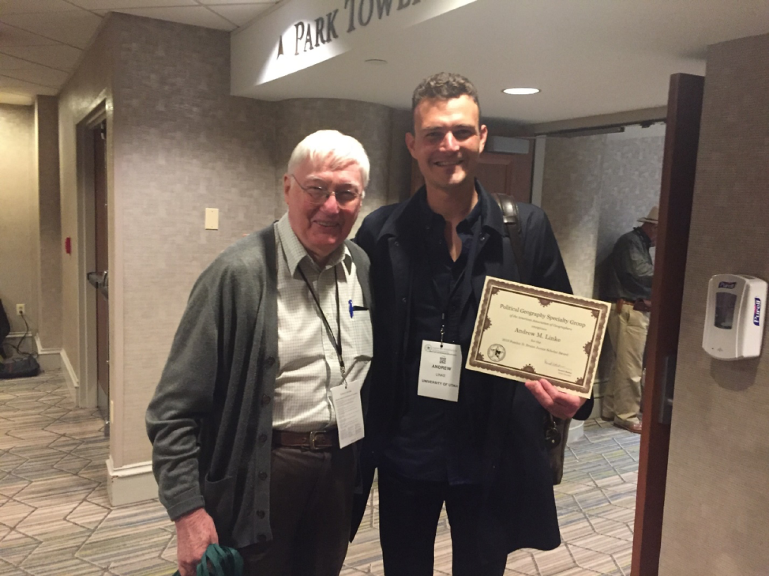 2 men posing with one displaying an award certificate