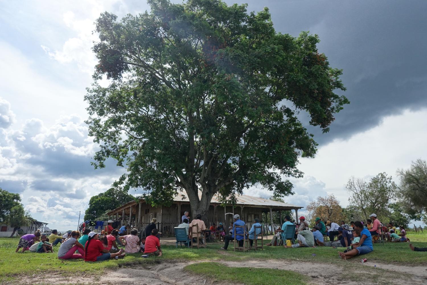 Group of indigenous people in Paraguay sitting under a tree in front of a building