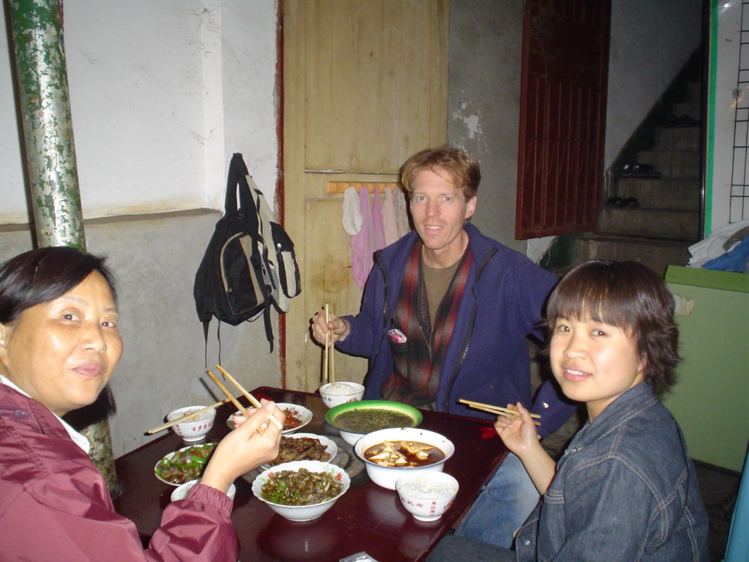 Caucasian man with chopsticks eating dinner with 2 Chinese women