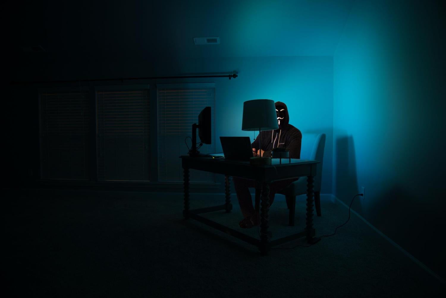 Hacker wearing a mask in dark room sitting at a computer