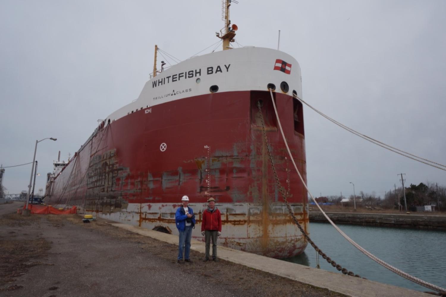 2 men on dock posing in front of large ship