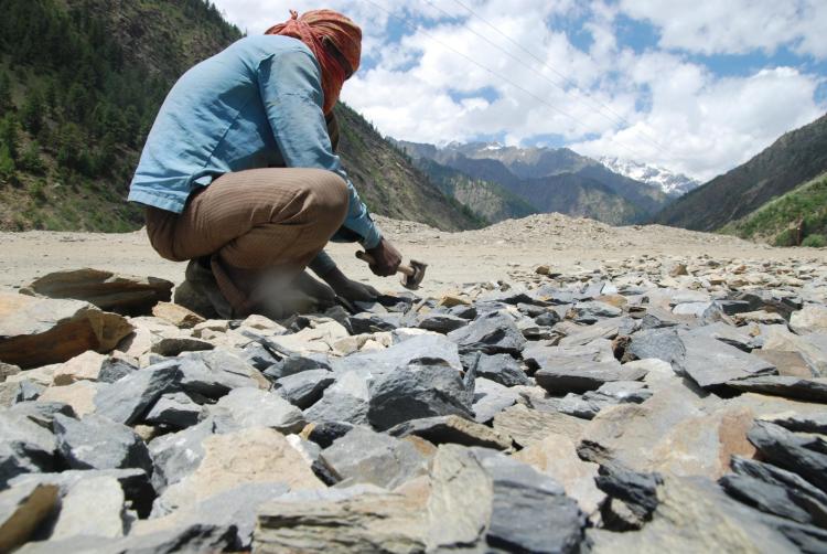 Person chipping rocks with a hammer in a mountain landscape