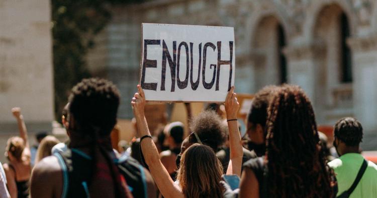 Crowd with one person raising a sign that says, "Enough".