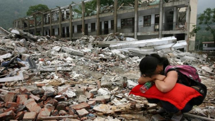 Woman squatting, burying head in arms, in front of earthquake devastation of Sichuan China