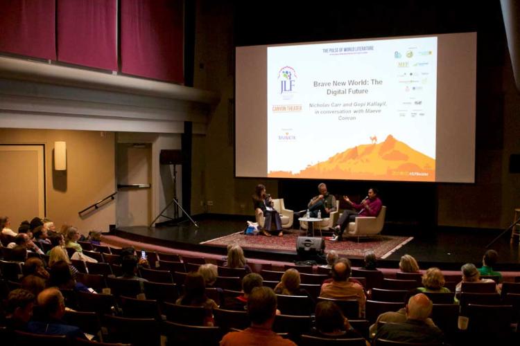 stage with 3 people sitting and a presentation screen behind them