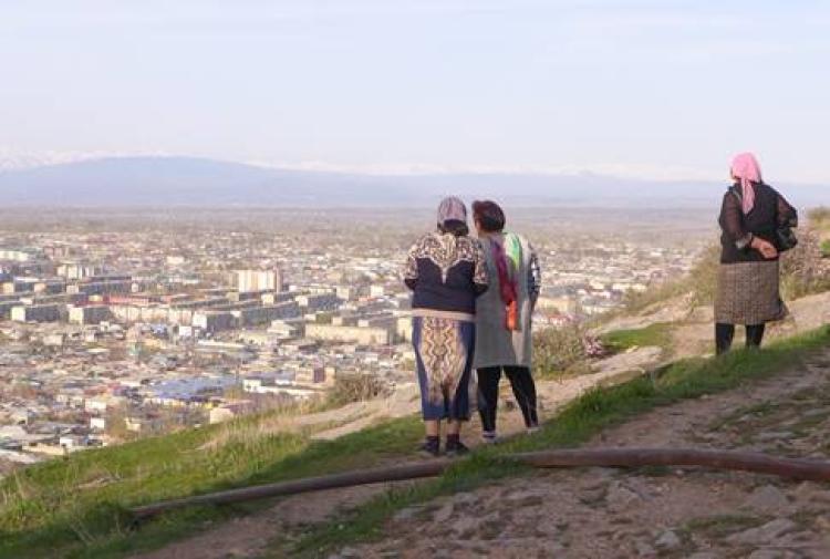 3 women standing on hill overlook a village
