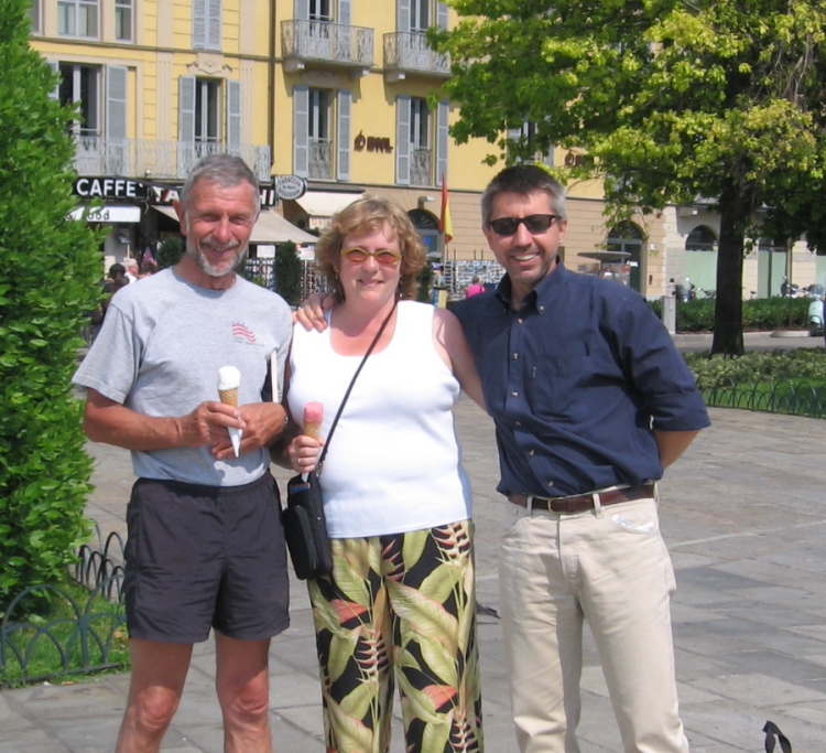 2 men and a woman holding ice creams cones, posing in a European town square.