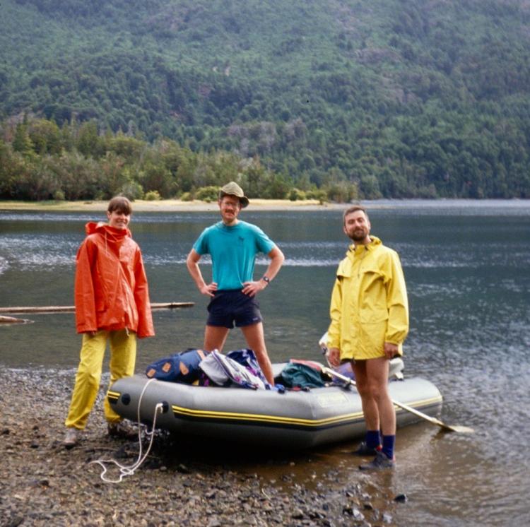 3 men posing in and near inflatable raft on a lake beach
