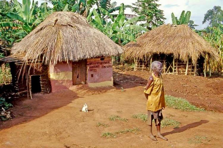 old man standing in front of thatched roof hut