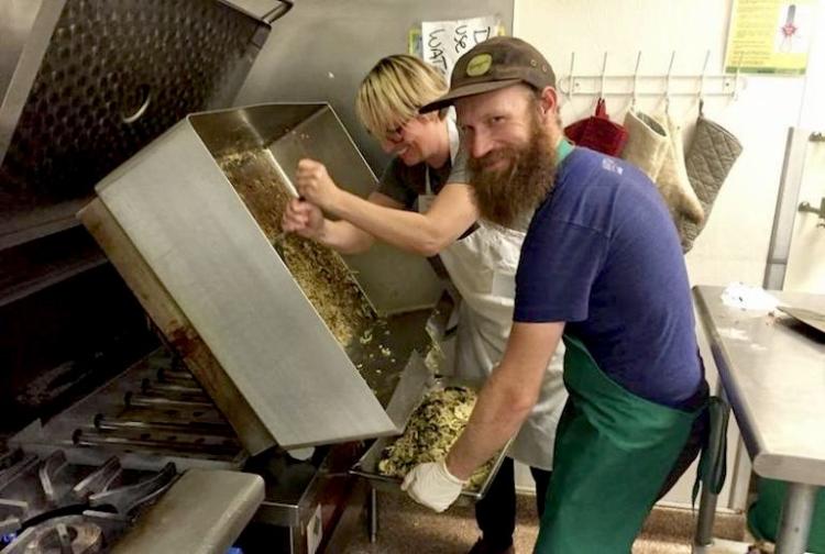 2 people cleaning a large griddle in a commercial kitchen