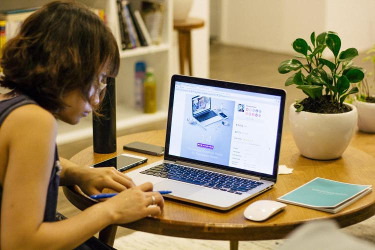 Female student holding pen sitting at table with laptop and mouse.