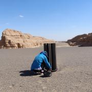 Woman squatting by research equipment in rocky desert-like landscape