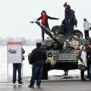 Non-military people climbing on tanks, posing for photos.