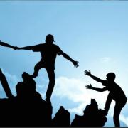 silhouettes of people helping each other climb a mountain