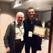 2 men posing with one displaying an award certificate