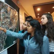 3 female students point to a wall-mounted aerial photo of a city