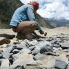 Person chipping rocks with a hammer in a mountain landscape