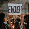 Crowd with one person raising a sign that says, "Enough".