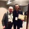 2 men posing with one displaying an award certificate