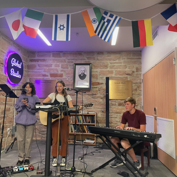 Three students performing at open mic night with guitar, singer, and piano