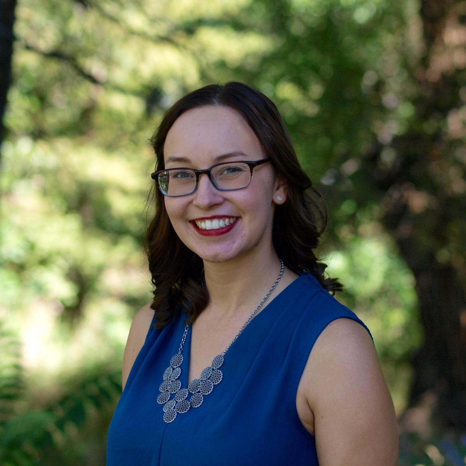 Headshot of Kellie in front of a leafy background