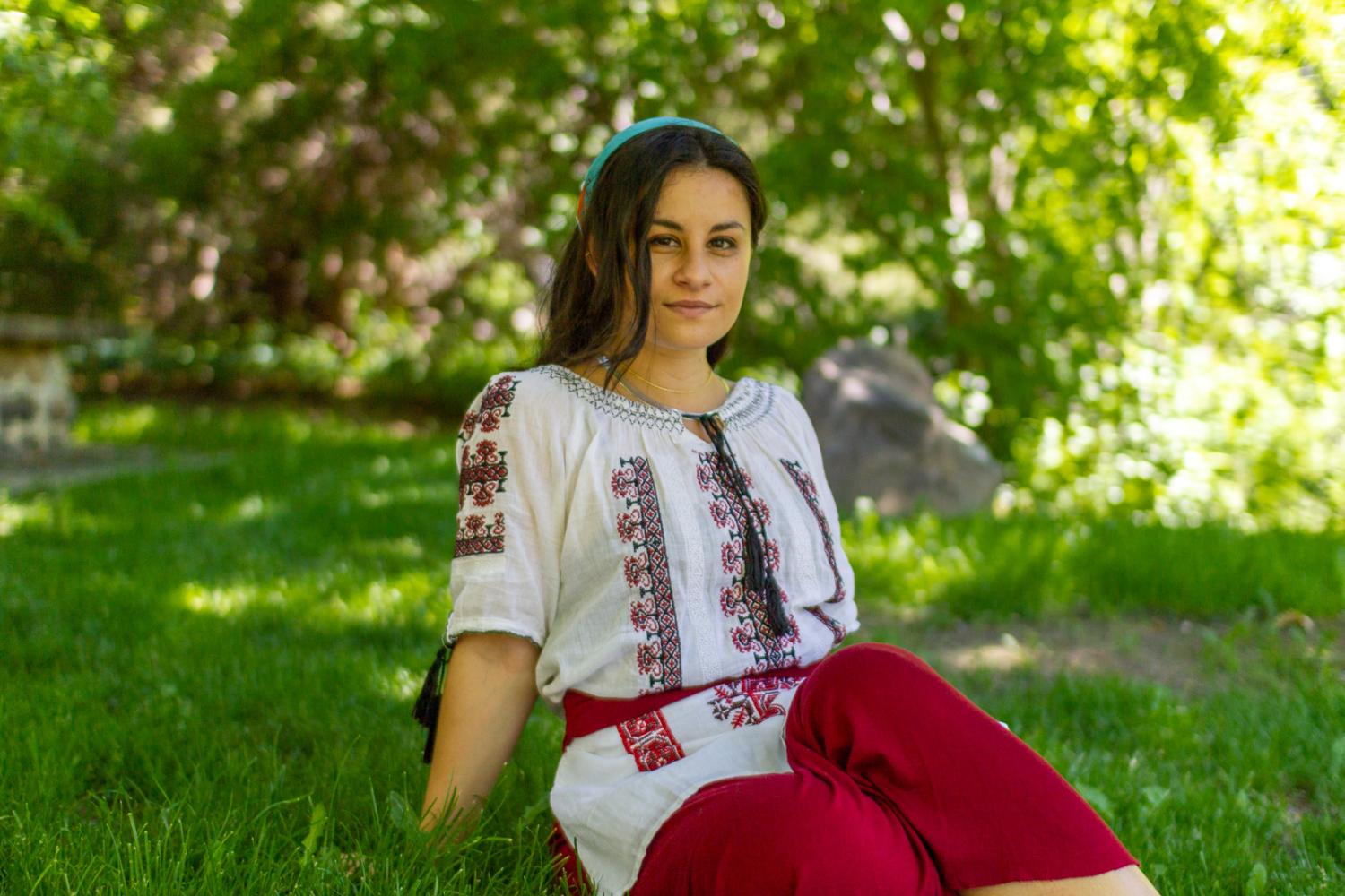 Dana sitting in the grass in front of green foliage