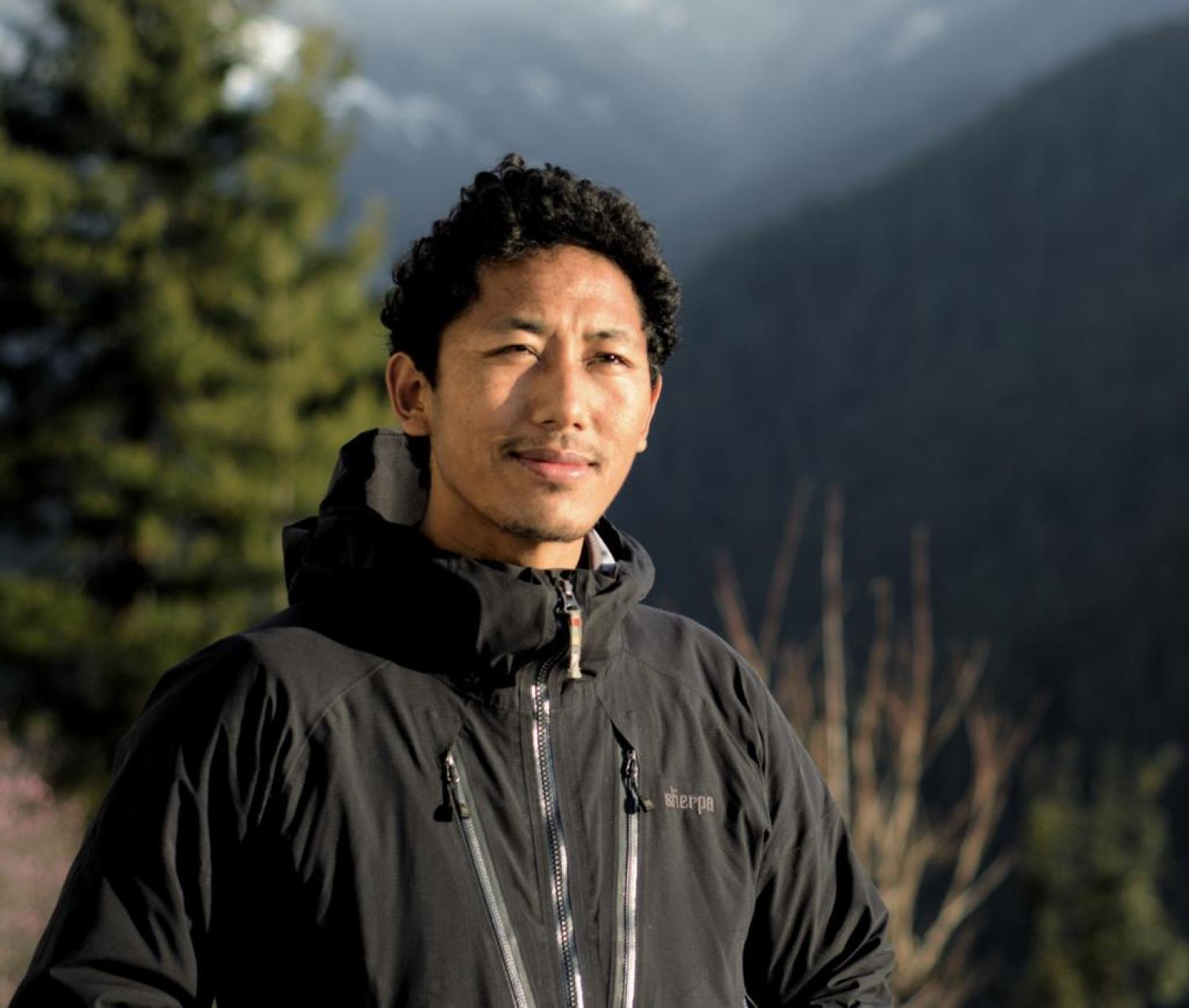 Phurwa in a black jacket in an outdoor landscape with many trees