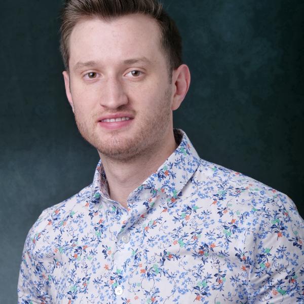 a headshot of a man with short brown hair wearing a light floral button down