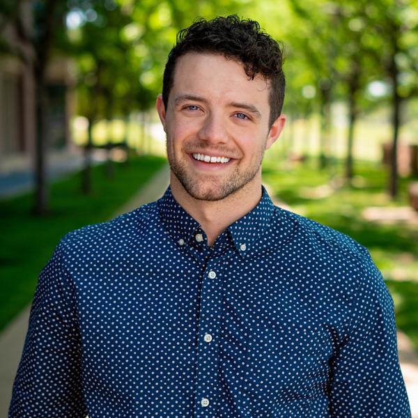 Ryan smiling in light colored printed shirt with a trees behind them. 