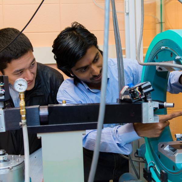 Student and faculty member looking at a piece of physics equipment in a lab