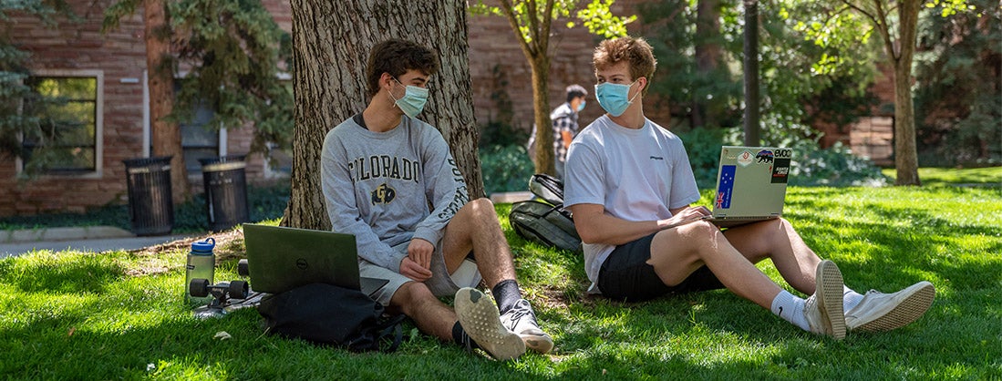 two students sitting outside on laptops