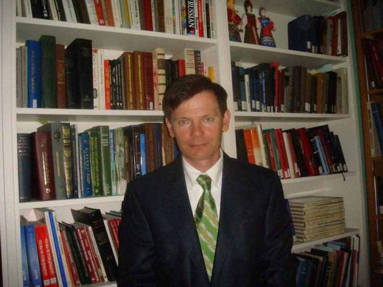 A photo of Artemi Romanov standing in front of a bookcase.