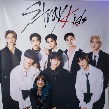 A photo of Sara standing in front of a poster of the kpop group, Stray Kids