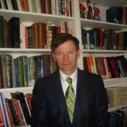 A photo of Artemi Romanov standing in front of a bookcase.