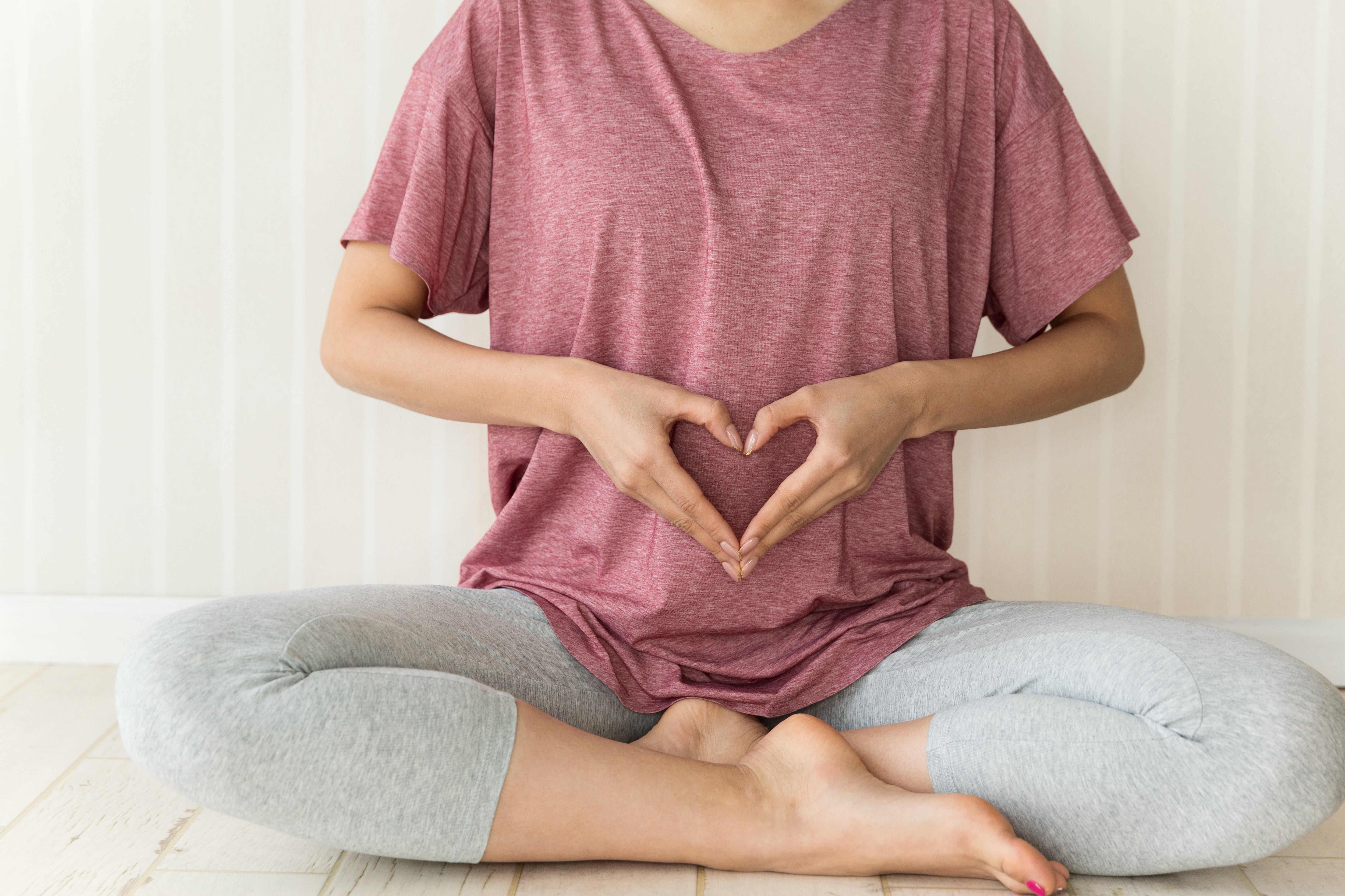 A woman holds her hands in a heart shape over her stomach