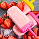 Strawberry popsicles on table surrounded by fresh strawberries. 