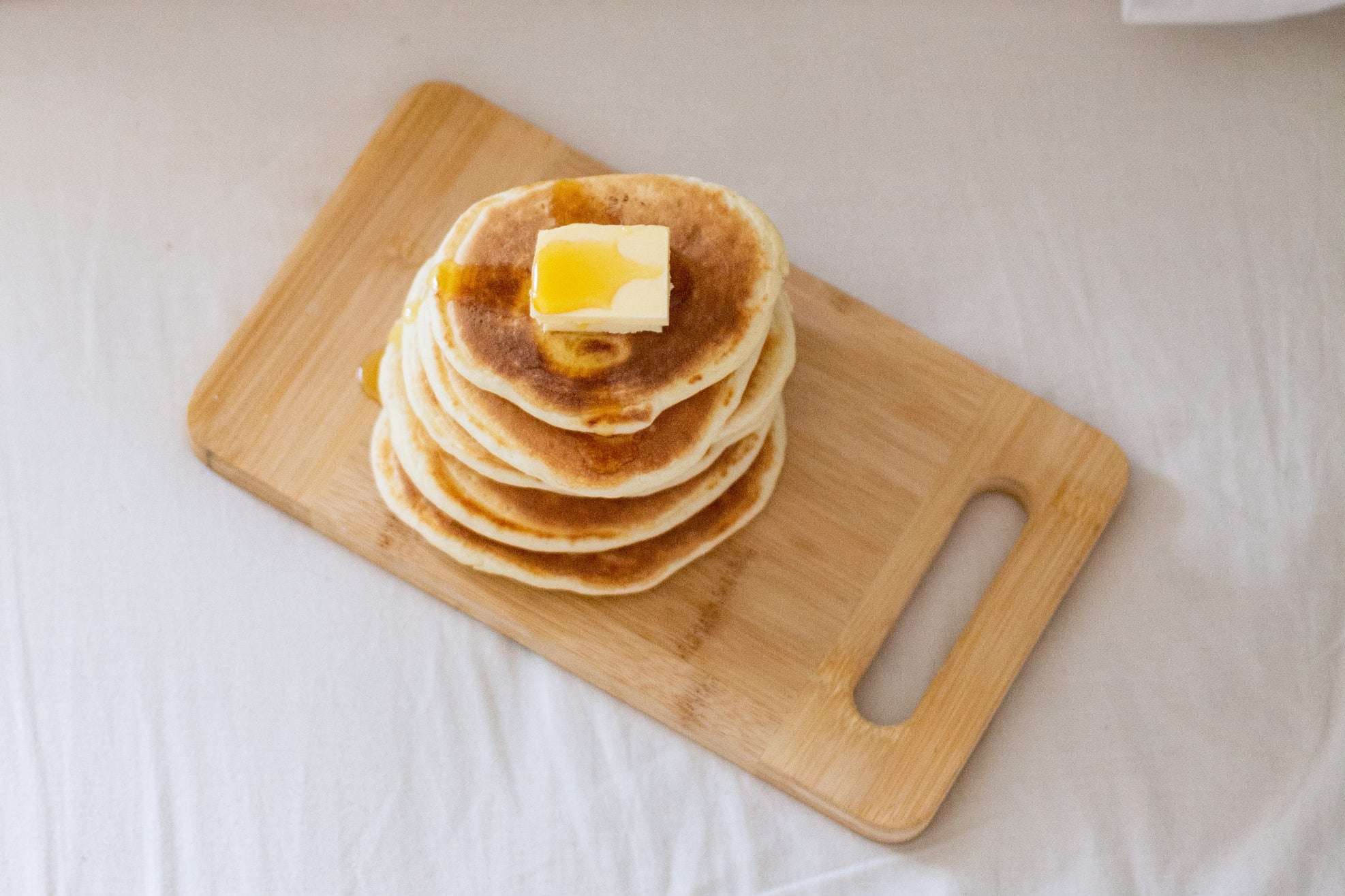 Stack of pancakes with syrup and button on top of a wooden cutting board.