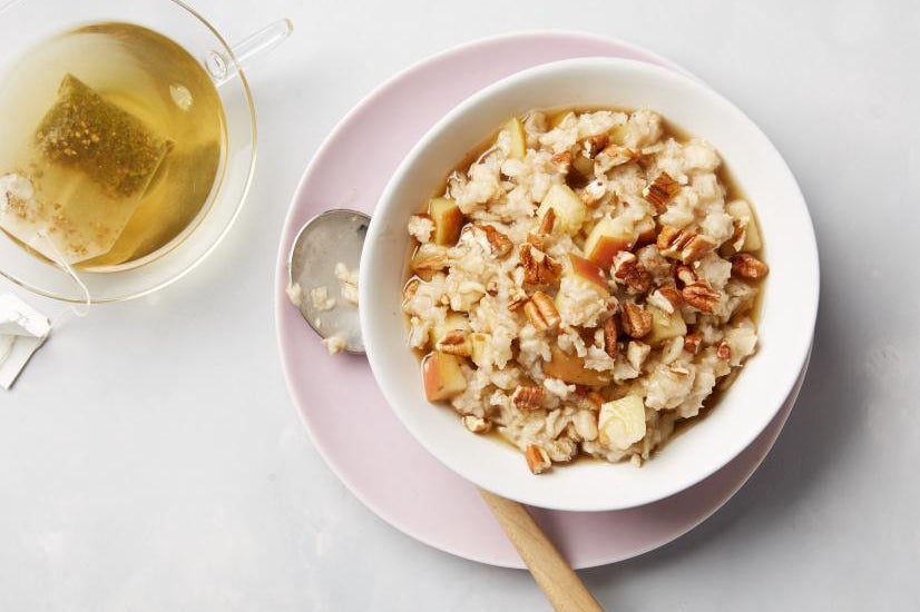 Bowl of oatmeal with nuts and other toppings next to a mug of tea.