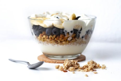 Clear bowl of yogurt, granola, peanut butter, berries and banana slices.