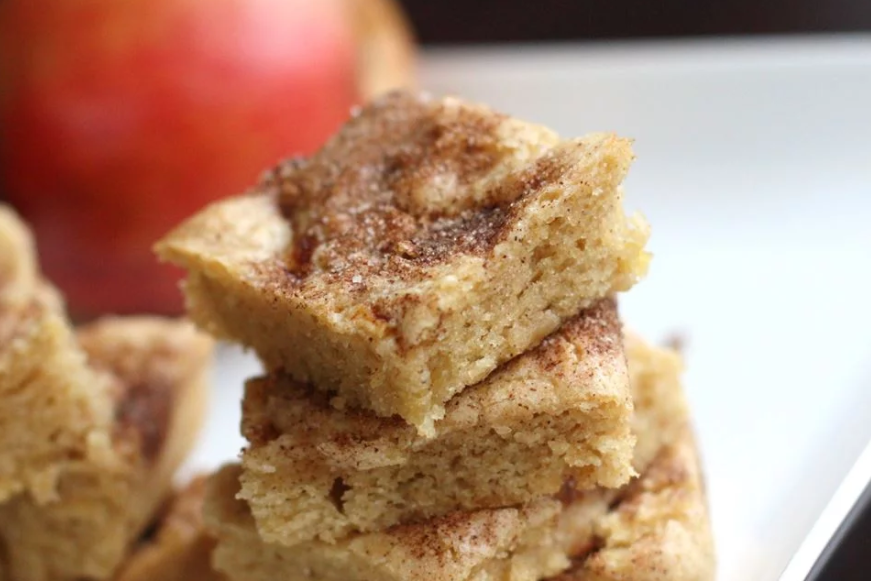 Stack of baked apple squares with apples nearby.