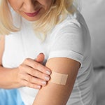 Photo of a woman applying a nicotine patch to her upper arm.