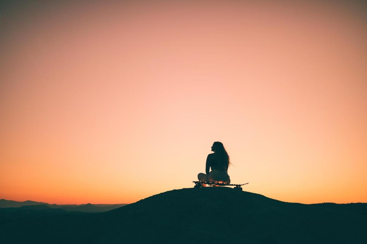 Photo of a girl sitting on a skateboard at sunset.