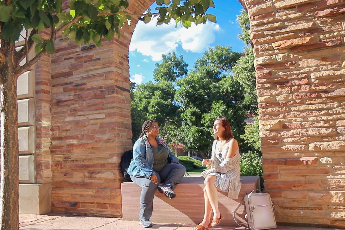 two women sitting under an arch talking