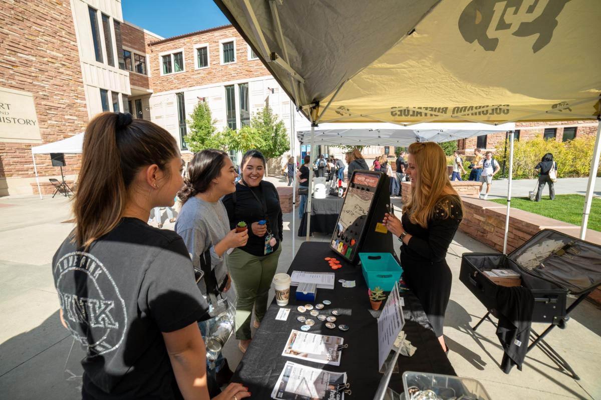 women talking at an outdoor booth during the take care street fair