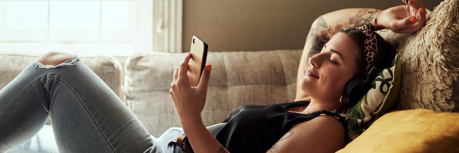 Student lying on the couch with headphones looking peacefully at her phone. 