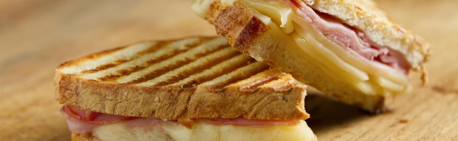 Two halfs of a grilled cheese and ham sandwich stacked on a wooden cutting board.