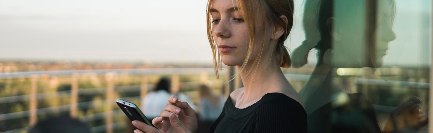 Photo of a student looking down at their phone while standing outside just before sunset.