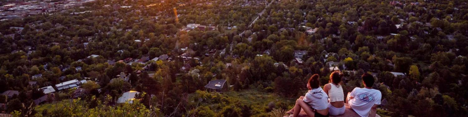 Photo of a three people sitting on a rock on Lookout Mountain with a scenic overview of Boulder.